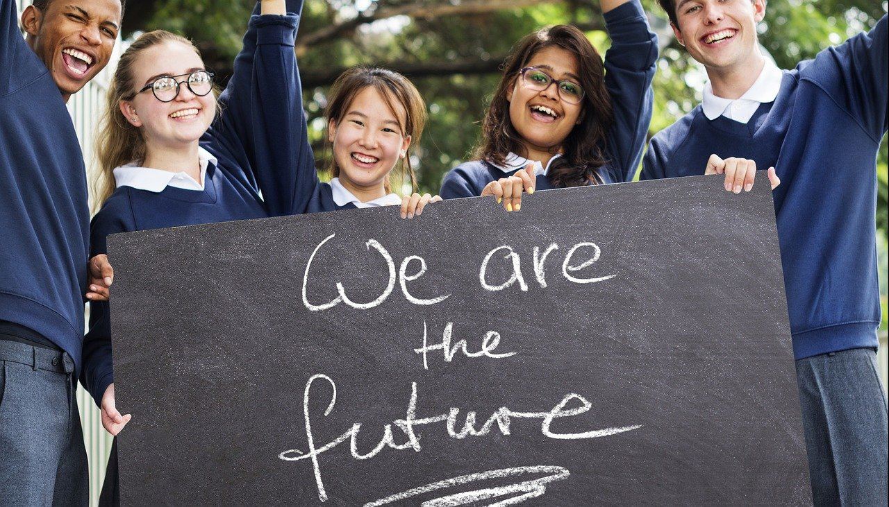 Five middle or high school students of mixed race, smiling and holding a sign that says "we are the future"
